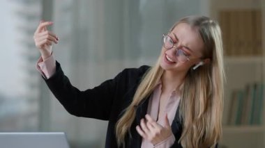 Kafkasyalı komik iş kadını kablosuz kulaklıkla müzik dinliyor gitar çalıyormuş gibi yapıyor gülümseyen iş kadını kız sesi dinliyor neşeli ofis özgürlüğü girişimcisi