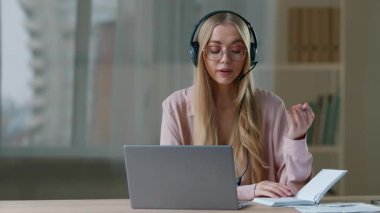 Kafkasyalı iş kadını, ofis işkadını şirketinde okuyan kulaklık takarak video konuşması yapıyor. Not defterinde yazan, sohbet eden, danışmanlık yapan kadın müşteri konferansı öğretmeni.