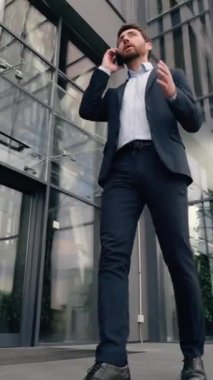 Kafkasyalı yetişkin iş adamı ofis binasının yanında yürüyor cep telefonuyla konuşuyor iş projesini tartışıyor akıllı telefon, iş adamı, şehir dışı iş adamı, şirket içi telefon görüşmeleri yapıyor.
