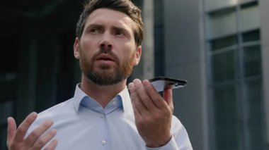 Kafkasyalı orta yaşlı iş adamı şehirde akıllı telefon mikrofonuyla konuşuyor. Hoparlör işadamı, erkek, cep telefonu işvereni ve dışarıdaki yetişkin adam iletişimini kullanarak sesli mesaj kaydediyor.