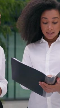 Afrikalı Amerikalı bir iş kadını elinde dosyasıyla Asyalı Koreli iş arkadaşlarını gösteriyor kadınlar proje planı verilerini tartışıyor kadın iş arkadaşları, şehir merkezindeki kızlar...