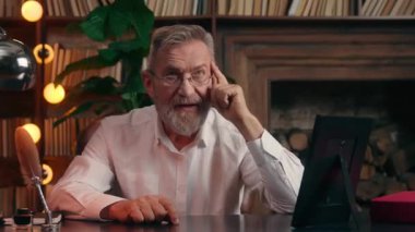 Düşünceli, düşünceli, Kafkasyalı bir iş adamı, yaşlı, yaşlı, yaşlı, erkek, emekli işadamı, masaya bakıp kameraya gülümseyen bir çözüm bulmayı düşünüyor.