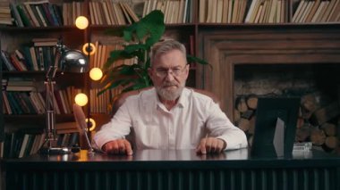 Ciddi, beyaz, yaşlı, kıdemli iş adamı ofis masasında el ele tutuşmuş yaşlı, yaşlı iş adamı yaşlı, erkek yönetici, kollarını kavuşturup kameraya bakıyordu.