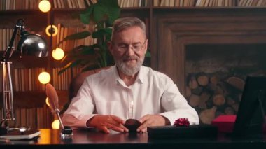Neşeli Kafkas kıdemli yaşlı iş adamı doğum günü pastasına mum üflüyor gülümsüyor akşam ofisindeki kamera portresine bakıyor emekli iş adamı erkek yöneticiler gülüşlerini kutluyor