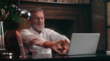 Kafkasyalı emekli iş adamı ellerini uzatarak dizüstü bilgisayarda çalışmaya başlıyor. Yaşlı, olgun, yaşlı işadamı. Ofiste bilgisayar teknolojisiyle çalışmaya hazırlanıyor.