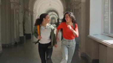 Üniversite koridorunda gülerek koşan iki mutlu kız öğrenci aktif sınıfa koşuyor gülümseyen kızlar, gülümseyen bayan arkadaşlar Latin Latin Latin çok ırklı kadınlar, derslere geç kalıyorlar.