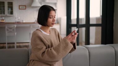 Mutlu İspanyol kadın kanepede gülüyor akıllı telefonlar çevrimiçi alışveriş yapıyor Latin kız nüfuzlu ev sahibi kiracı cep telefonu sosyal medya sohbetleri yapıyor internet rezervasyonları yapıyor.