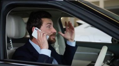 Heyecanlı Kafkasyalı iş adamı araba galerisinde cep telefonuyla konuşuyor. Zaferi kutluyor. Erkek sürücü alıcısı.