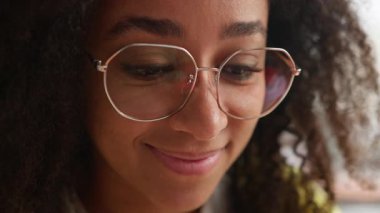 Mutlu bir portre Afro-Amerikan üniversiteli kız öğrenci yüzü aşağı bakıyor heyecanlı bir gülümseme neşe saçan bir kadın kolejde kapalı alanda etnik bir kadın gibi görünüyor liseli iş kadını neşeli