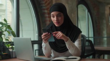 Müslüman İslami iş kadını, tesettürlü kadın iş kadını. Düşünceli, daktilo çeken, cep telefonlu, fikir alışverişi yapan, akıllı telefonlu, gülümseyen, iyi haberler alan, ofiste kazanmayı başaran.