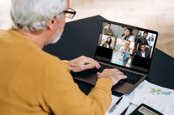 Video call communication. Elderly caucasian man is using a laptop for distant online studying, he looks at the laptop screen on which the teacher and other participants of the video conference