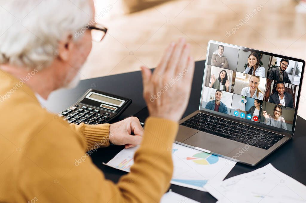Video conference. Business partners communicate via video conference using laptop. The old gray-hair man talks with his business partners and waving hand. Distant work