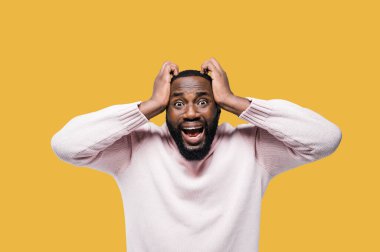 Afrika kökenli Amerikalı bir adamın duygusal portresi. Yüksek sesle bağırıyor, kameraya bakıyor, ellerini başının üstüne koyuyor, portakallı arka planda duruyor. Stresli ya da korkmuş.