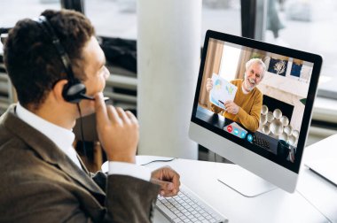 Video iletişimi. Başarılı bir iş adamı ya da kulaklıklı bir yönetici, olgun iş arkadaşlarıyla finansal grafikler ve stratejiler ve video görüşmeleri ile diğer çalışma anlarını tartışıyor. 