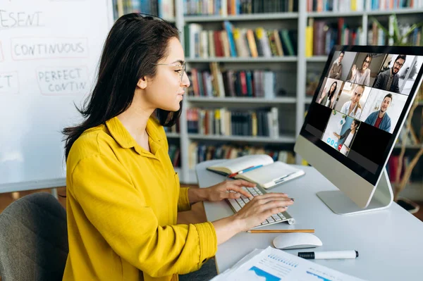 オンライン教育 女性学生が自宅でオンラインで学び 他の学生や教師のグループが情報を伝えるコンピュータモニタを見ることに焦点を当てた — ストック写真