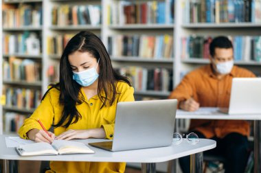 Karantina sırasında eğitim. Öğrenciler birbirlerinden uzak otururlar, yüzlerinde koruyucu maskelerle ve dizüstü bilgisayarla çalışırlar.