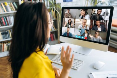 Çok ırklı uluslararası iş arkadaşlarıyla birlikte gelecekteki mali planlar ve strateji hakkında tartışan grup video görüşü sırasında bilgisayar monitörü kadın omuz üzerinden görüşü