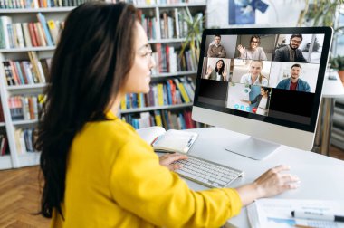 Çevrimiçi öğrenme. Online ders sırasında bir kız öğrenci diğer öğrencilerin ve bir öğretmenin ders verdiği monitöre bakar.