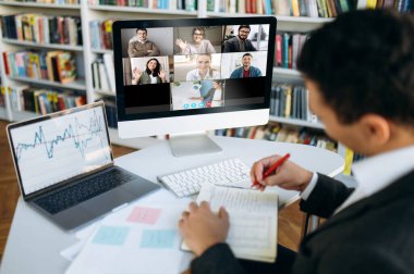 Çevrimiçi video konferansı. Başarılı genç iş adamı iş arkadaşlarıyla finansal grafikler ve strateji üzerine tartışan bilgisayarla video aracılığıyla iletişim kuruyor.
