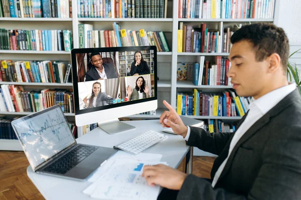 Online video meeting. Successful young adult businessman communicate with  business colleagues by video call using computer discussing about financial graphs and strategy