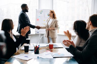 Pazarlıktaki iş ortakları. Çok ırklı takımlar brifingde anlaştılar. Afrikalı Amerikalı erkek patron, beyaz kadın meslektaşıyla el sıkışıyor, bir sözleşme imzalıyor, işbirliği konsepti oluşturuyor.