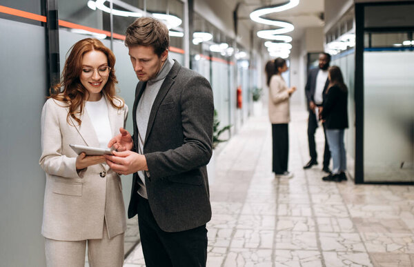 Caucasian business partners at the workplace. Friendly colleagues cooperate to develop a startup or project together. Handsome man ask for advice from beautiful smiling woman, collaboration concept