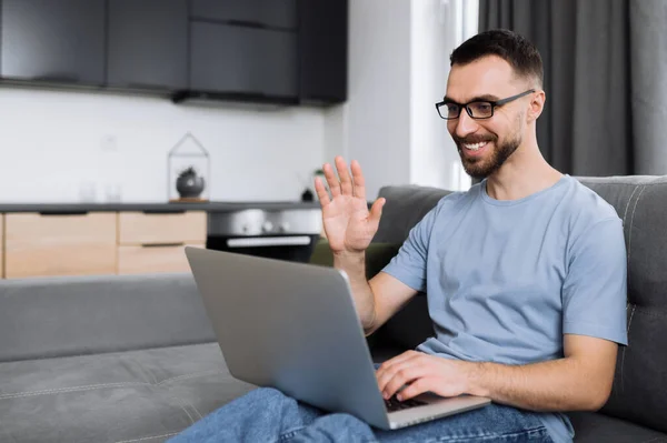 Videosamtal. Glada manliga frilansare använder laptop, har ett videosamtal, kommunicera med kollegor eller vänner genom videokonferens, viftande hand och leende. Snygg affärsman sitter på en — Stockfoto