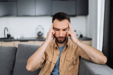 Kafkas sakallı yorgun adam koltukta oturuyor ve başı ağrıyor. Sağlıksız bir adam soğuk algınlığına yakalanır veya grip olur, hastalığa üzülür, mutsuz bir adam depresyona girer.