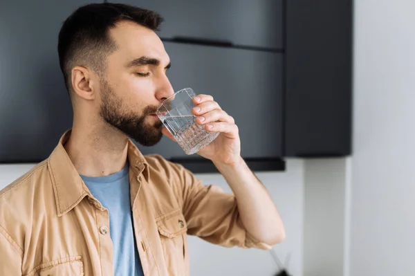 Caucasian attractive male drinking a pure water, follow healthy lifestyle. Cheerful man recommending drink daily amount of pure liquid. Handsome guy feel thirsty, dehydration concept