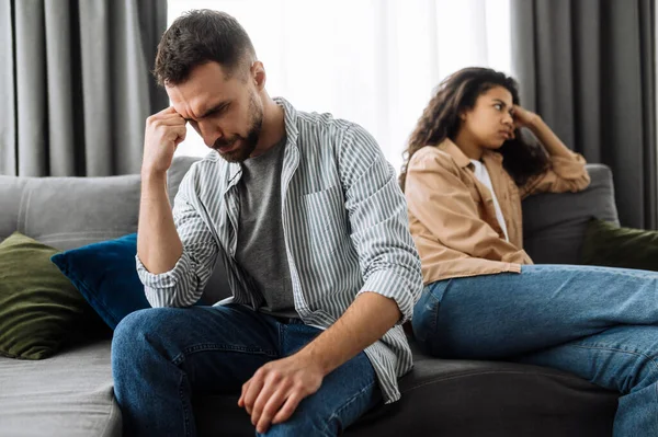 Perselisihan antara sepasang kekasih. Seorang pria yang kesal dan seorang gadis yang tersinggung dan mengabaikan satu sama lain sambil duduk di sofa, berpaling ke arah yang berbeda — Stok Foto