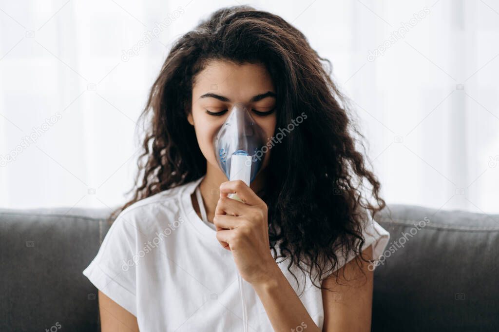 Close-up photo of sick african american woman with an inhaler. Unhealthy millennial girl doing inhalation at home, she use nebulizer and inhaler for the treatment. Cough and flu