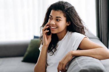 Güzel Afrikalı Amerikalı kız evdeki kanepede oturuyor. Çekici genç bir kadın telefonda arkadaşıyla, ailesiyle ya da erkek arkadaşıyla konuşuyor, başka tarafa bakıyor ve gülümsüyor. Evde boş zaman.
