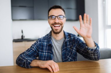 Video konferansı sırasında mutlu bir beyaz adamın portresi, kameraya bakıp el sallıyor ve gülümsüyor, arkadaşlarını, ailesini ya da meslektaşlarını selamlıyor.