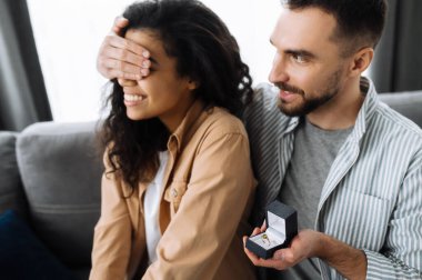 Oturma odasındaki kanepede birbirine aşık çok ırklı bir çift. Adam, sevgili kız arkadaşının gözlerini kapatıyor ve ona bir yüzük verip evlenme teklifi etmeye hazırlanıyor..