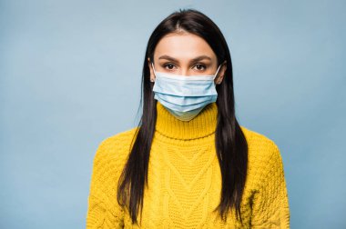 Karantina sırasında Coronavirus covid-19 'un steril yüz maskesi takan sarı kazaklı esmer kadının portresi doğrudan kameraya bakıyor.