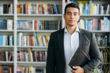 İş yerinde resmi giyinmiş İspanyol bir adamın portresi. Başarılı erkek menajer kameraya bakıp gülümsüyor. Modern ofiste nüfuzlu bir işadamı olarak, kendine güvenini göster.