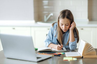 Uzaktan öğrenme, karantina sırasında evde eğitim. Kafkasyalı güzel kız ödevini evde yapıyor, laptopunu kullanıyor, çalışma masasında oturuyor.