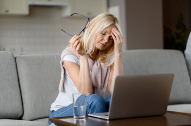 Üzgün, orta yaşlı, serbest çalışan, internette fazla çalışmaktan bıkmış, oturma odasında oturuyor, gözlüklerini çıkarıyor, gözlerini kapıyor, dinlenmeye ihtiyacı var.