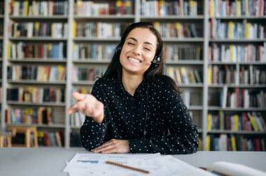Mutlu kadın çalışanın webcam portresi. Video konferansındaki neşeli iş kadını, kulaklık takıyor, gülümsüyor, kameraya bakıyor, elle hareket ediyor, iş arkadaşlarıyla iletişim kuruyor.