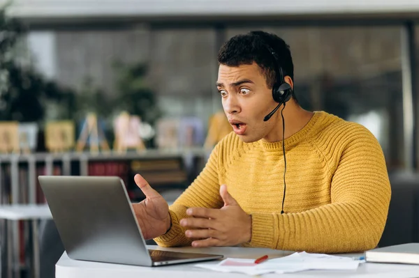 Worried employee having a problem with internet connection while important video meeting. Confused male manager sit at the desk, using computer, upset about work issues