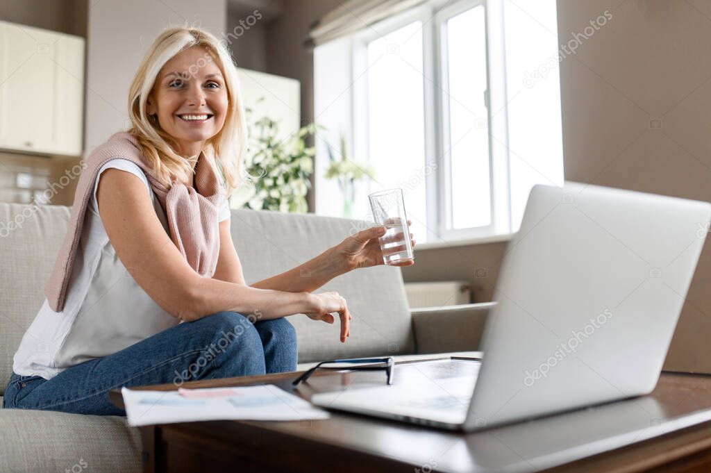 An adult woman follows a healthy lifestyle. Busy successful business woman taking a break from distance work or learning, drinking water while working or studying process