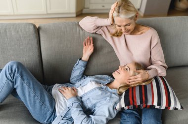 Anne-kız ilişkisi. Olgun anne ve genç yetişkin kız evlerinde kanepede sohbet ediyorlar, sırlarını paylaşıyorlar, anne kızına tavsiye veriyor.