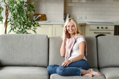 Gülümseyen orta yaşlı kadın akıllı telefon kullanır, arkadaşlarıyla ya da ailesiyle konuşur. Kıdemli kadın, günlük kıyafetler içinde koltukta oturuyor, cep telefonuyla konuşuyor, gülümsüyor, iletişim konsepti kuruyor.