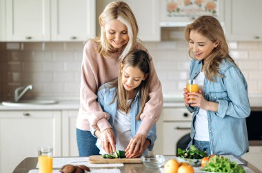 Üç nesil boyunca kadınlar mutfakta birlikte vakit geçirir, büyükannem torununa salata kesmeyi öğretir ve annem gülümseyerek meyve suyu içer.