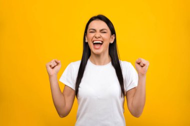 Mutlu, beyaz tişört giyen, başarıyla sevinen ya da kazanan, mavi izole edilmiş arka planda duran mutlu beyaz kız.