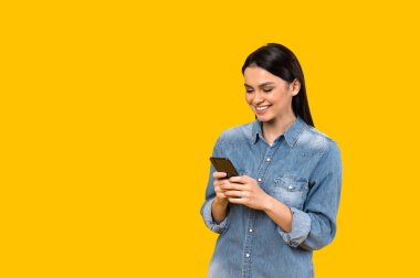 İnternette sohbet ediyoruz. Beyaz kız akıllı telefonunu kullanarak mesajlaşıyor, arkadaşlarına ya da erkek arkadaşına mesaj yazıyor, izole edilmiş turuncu arka plana karşı duruyor ve gülümsüyor.