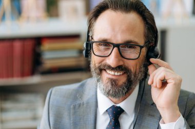 Çağrı merkezinin orta yaşlı, sakallı, memnun operatörünün yakın plan portresi. Kafkasyalı işadamı kameraya bakıyor ve gülümsüyor.