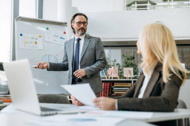 Resmi takım elbiseli kendinden emin kıdemli işadamı, şirket için yeni bir strateji hakkında konferansta bir sunum yapacak. Yakışıklı erkek çalışan, iş raporunu sarışın bayan meslektaşına sunar.