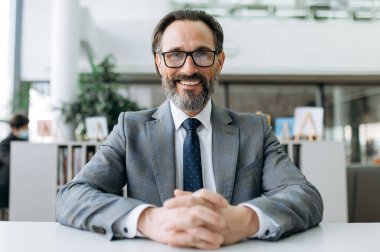 İş yerinde başarılı, neşeli, olgun bir iş adamının portresi. Gözlüklü, yaşlı ve nüfuzlu bir adam hakkında webcam görüşü masada oturup, video brifinginde iş arkadaşlarıyla iletişim kuruyor.