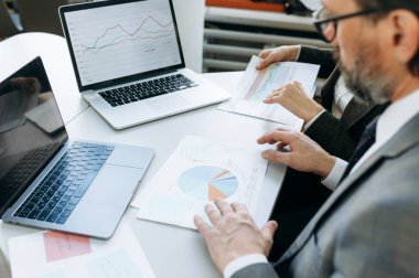 Evrak işleri yapan, finansal grafikler ve diyagramlar öğrenen iş adamlarına yakın çekim. - Modern ofisteki masada oturan kıdemli yetişkin işveren proje için belgelerle çalışıyor.